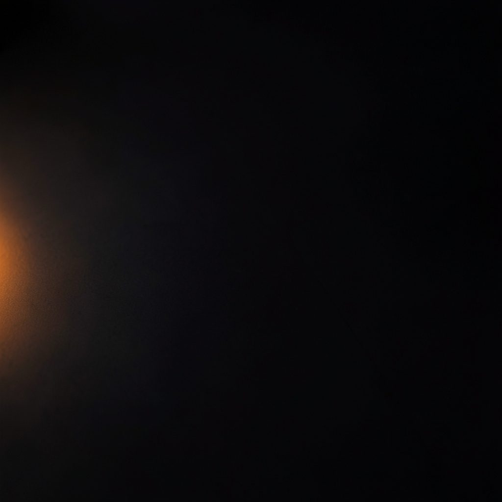 Dark photograph of a smooth charcoal surface with a faint warm glow along one edge, minimalist and elegant