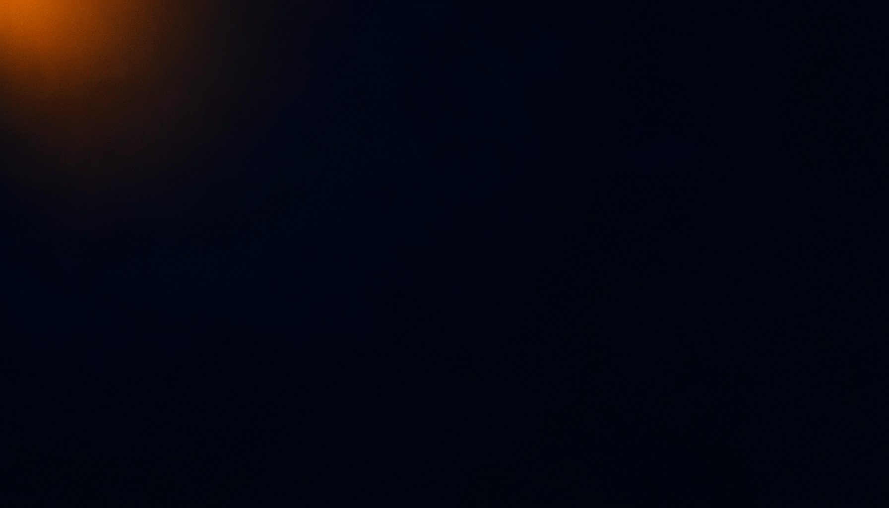 Dark atmospheric photograph with deep navy shadows and subtle warm amber light bleeding from the top left corner, creating a moody, sophisticated backdrop
