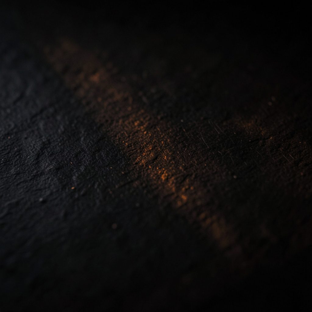 Dark photograph of a textured charcoal surface with subtle warm highlights, moody and refined