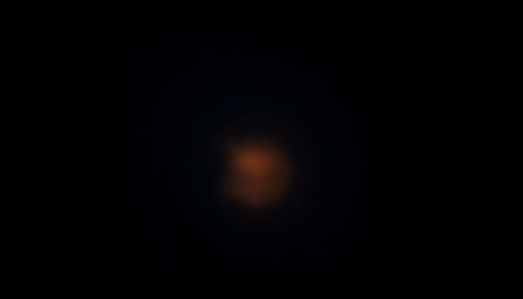 Dark low-key photograph of deep navy and charcoal tones with a subtle warm amber glow near the center, atmospheric and dramatic